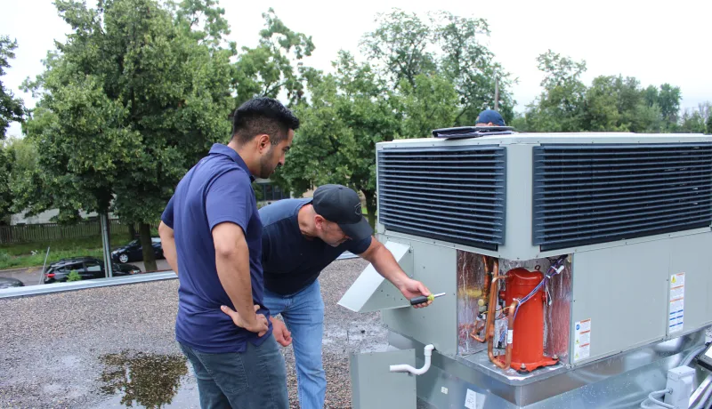 Two people looking at the inside of HVAC equipment. 